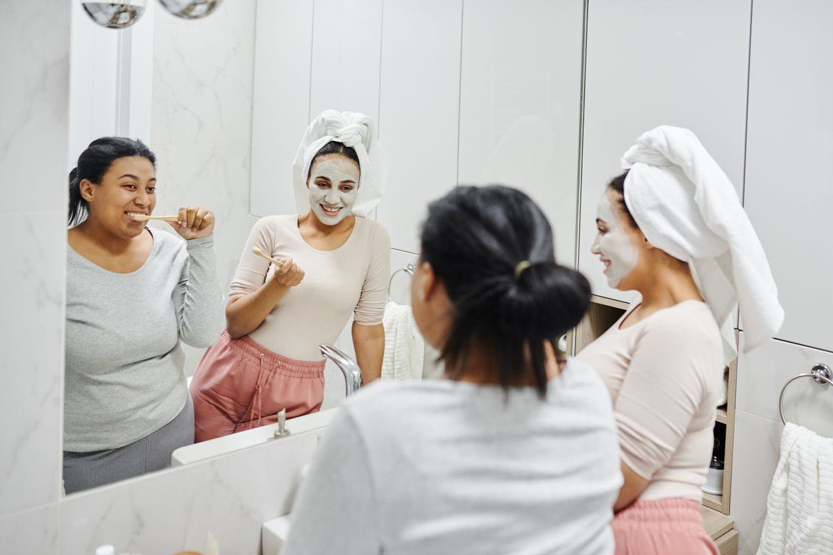 Two women laughing while brushing their teeth