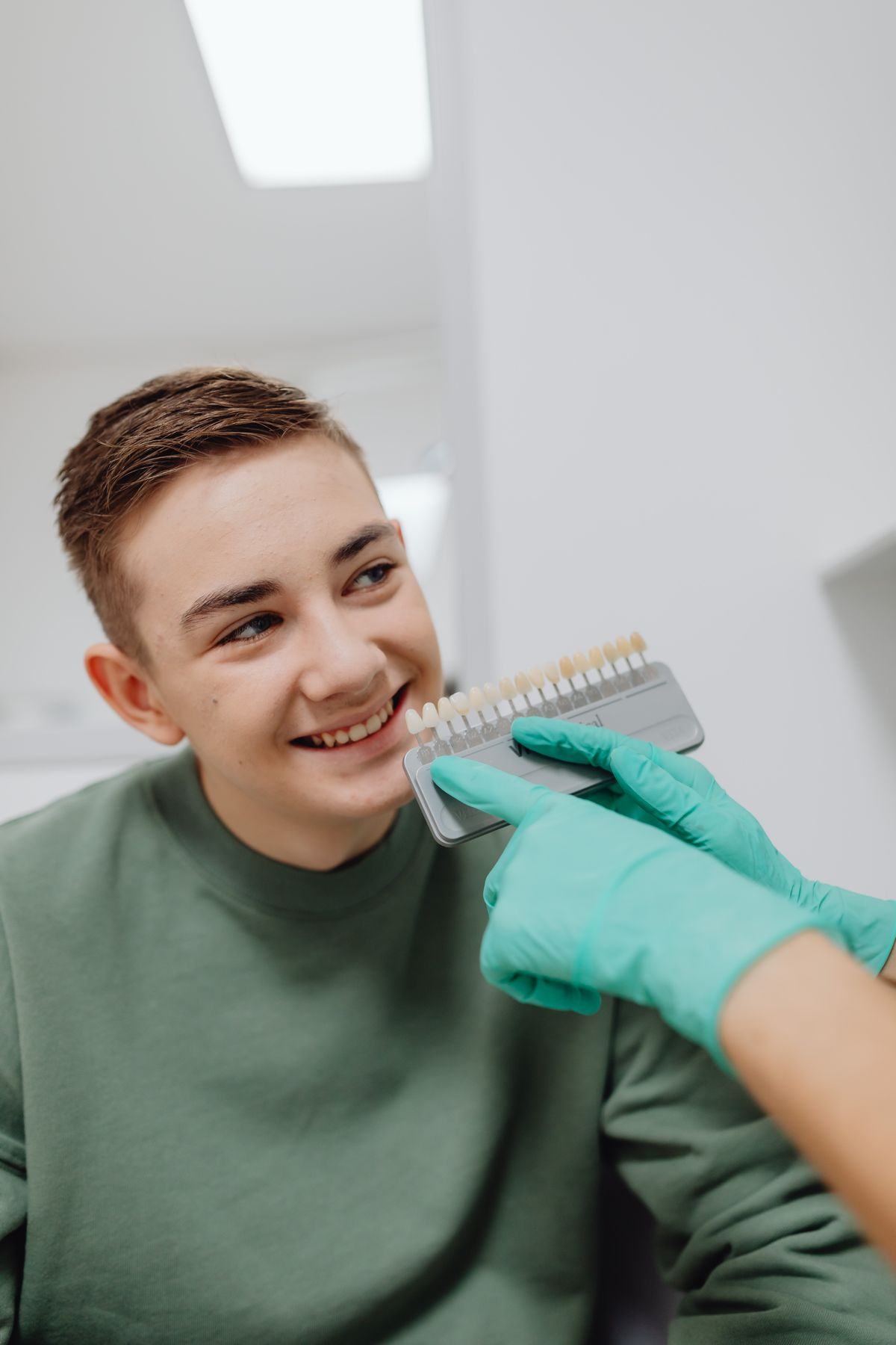 A smiling teenager checking a tooth shade with a dentist